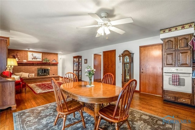 dining space with a ceiling fan, a brick fireplace, dark wood finished floors, and brick wall