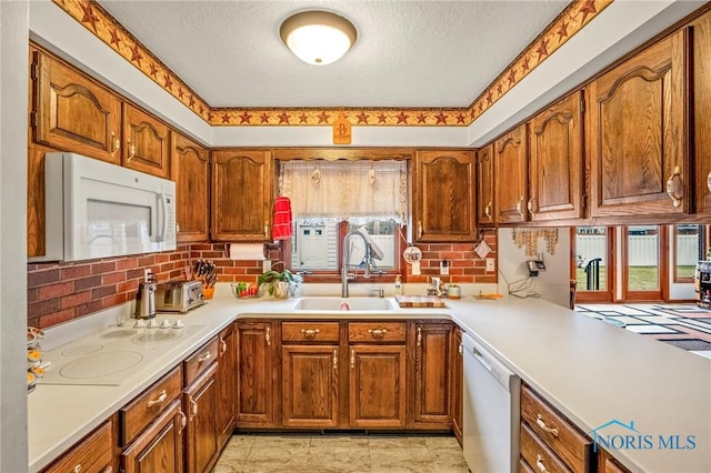 kitchen featuring a sink, a textured ceiling, white appliances, brown cabinetry, and light countertops