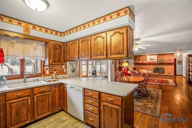 kitchen with brown cabinets, a sink, a peninsula, a fireplace, and dishwasher