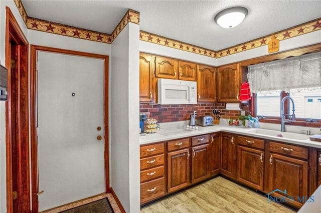 kitchen featuring white appliances, brown cabinetry, a sink, decorative backsplash, and light countertops