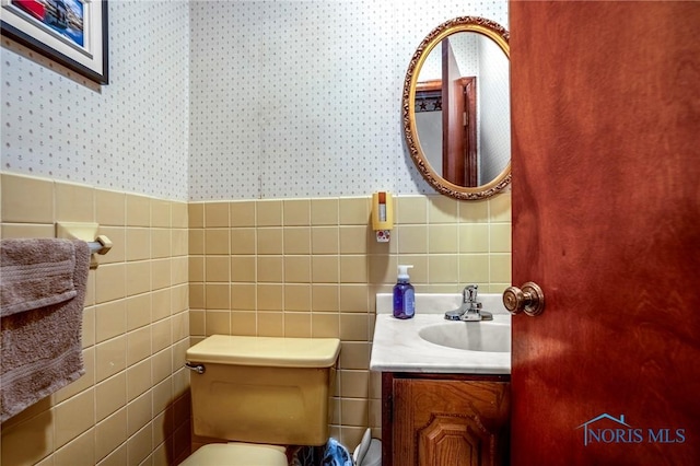 half bath featuring wallpapered walls, tile walls, toilet, and vanity