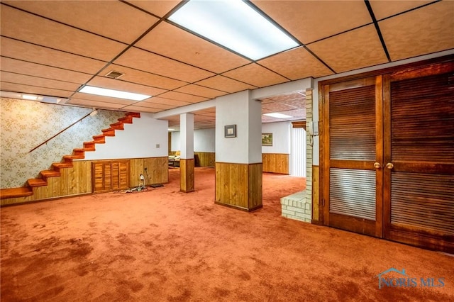 finished basement with carpet, a wainscoted wall, and a paneled ceiling