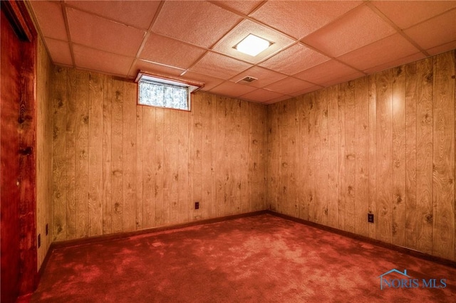 basement with a paneled ceiling, wood walls, and carpet flooring