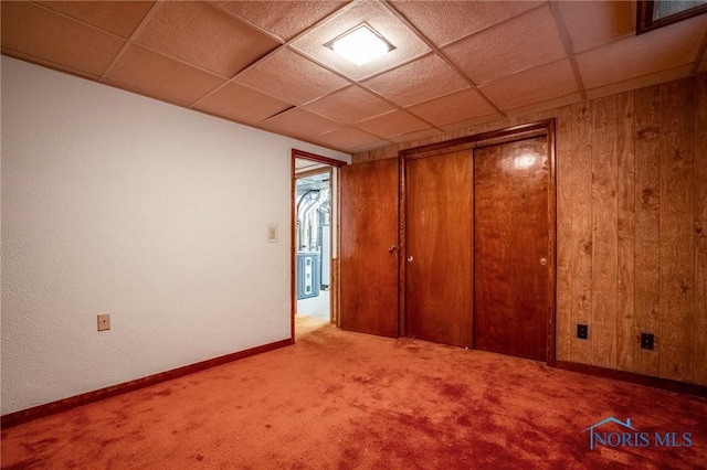 unfurnished bedroom featuring carpet flooring, wood walls, a paneled ceiling, and baseboards