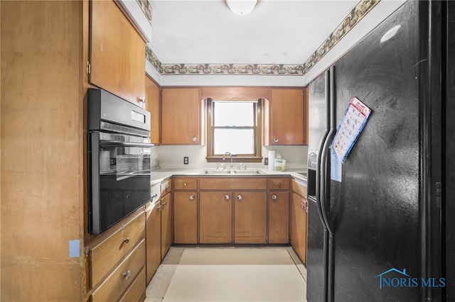 kitchen with brown cabinetry, black appliances, light countertops, and a sink