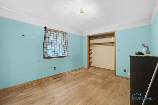 unfurnished bedroom with hardwood / wood-style flooring, baseboards, a closet, and a textured ceiling