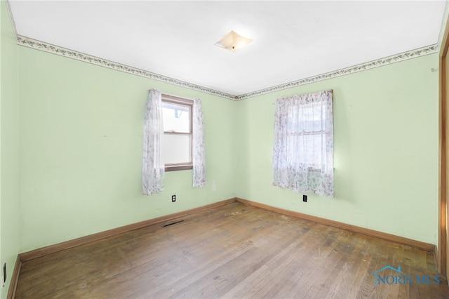 spare room with hardwood / wood-style flooring, baseboards, and visible vents