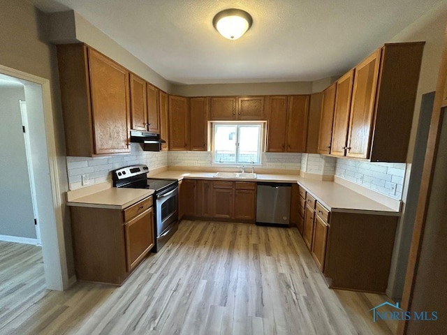 kitchen featuring a sink, light wood-style floors, under cabinet range hood, appliances with stainless steel finishes, and tasteful backsplash