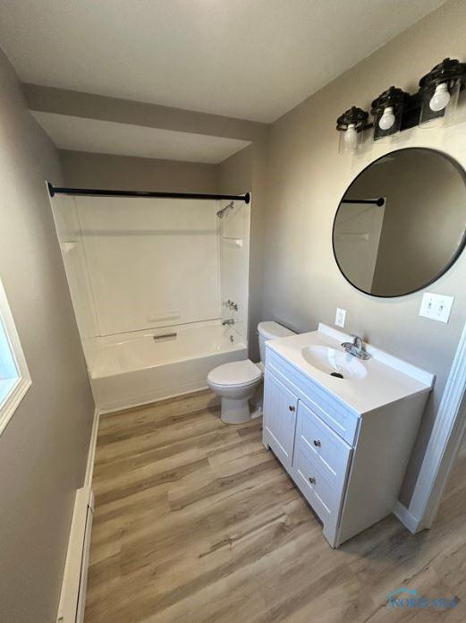 full bath featuring vanity, wood finished floors, shower / bath combination, toilet, and baseboard heating