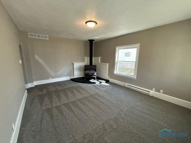 unfurnished living room with baseboards, visible vents, a baseboard radiator, a wood stove, and dark colored carpet