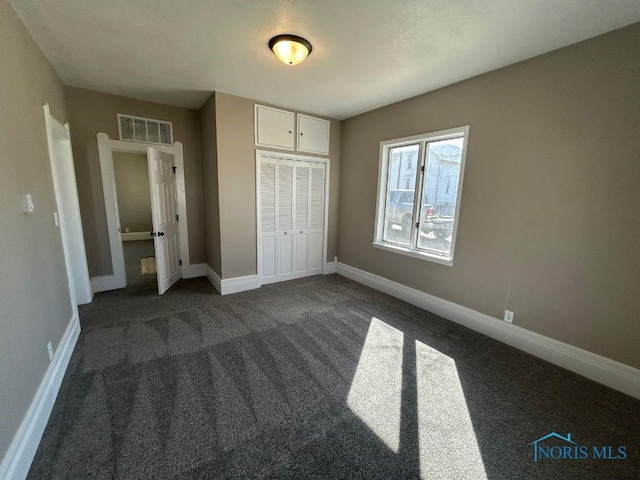 unfurnished bedroom with dark colored carpet, visible vents, baseboards, and a closet