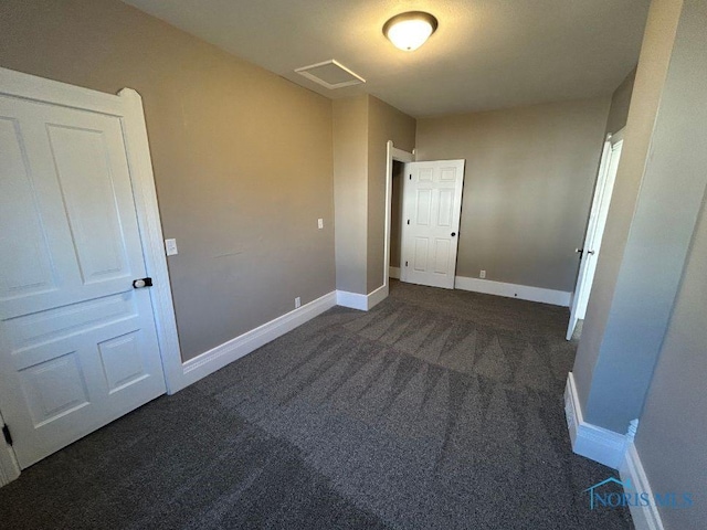 empty room featuring visible vents, dark carpet, and baseboards