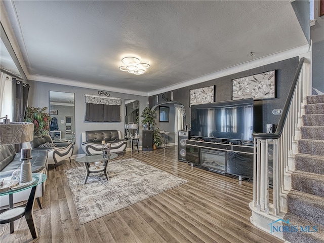 living room featuring arched walkways, crown molding, stairs, and wood finished floors