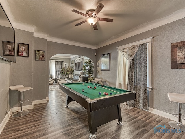 recreation room with arched walkways, wood finished floors, and a textured wall