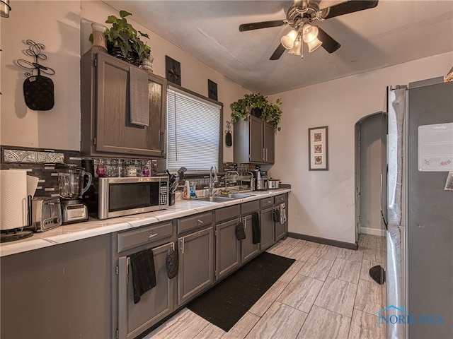 kitchen with light countertops, decorative backsplash, arched walkways, stainless steel appliances, and a sink