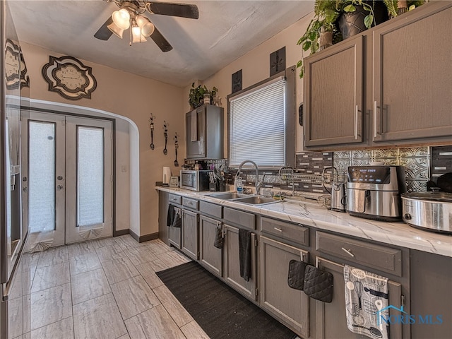 kitchen with baseboards, decorative backsplash, french doors, arched walkways, and a sink