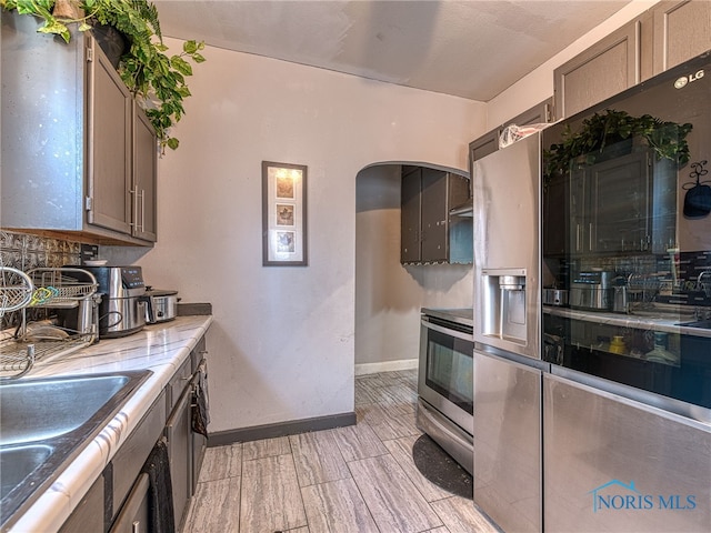 kitchen featuring gray cabinetry, arched walkways, stainless steel electric range, baseboards, and wood tiled floor