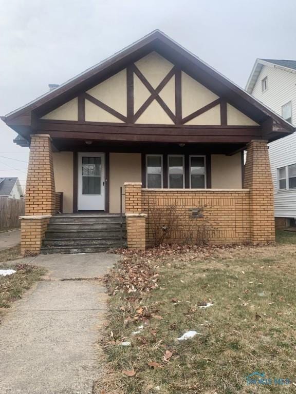 view of front of house featuring brick siding, covered porch, and stucco siding