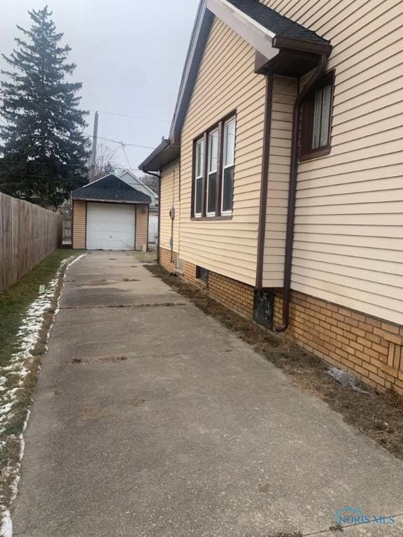 view of side of home featuring a detached garage, an outdoor structure, concrete driveway, and fence