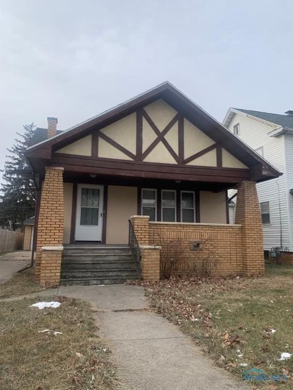 view of front of house with brick siding, a chimney, covered porch, and stucco siding