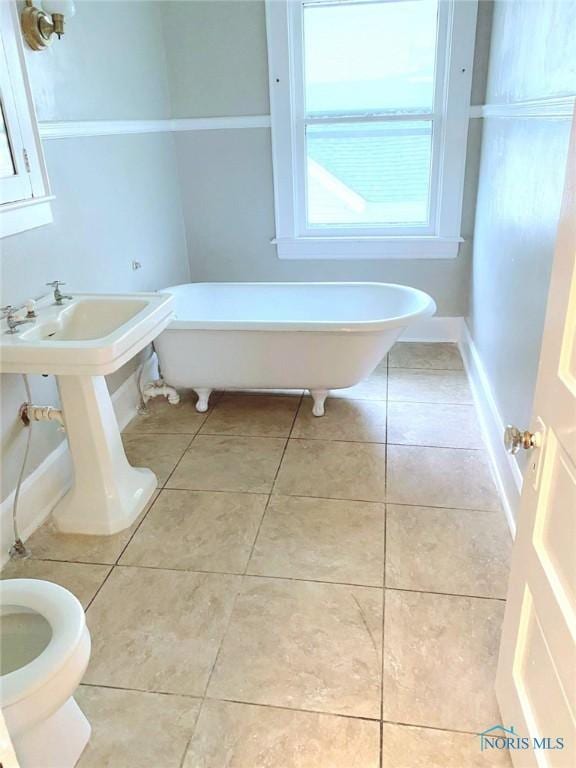 bathroom with tile patterned floors, toilet, baseboards, and a freestanding bath