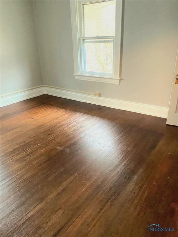 spare room with baseboards and dark wood-type flooring