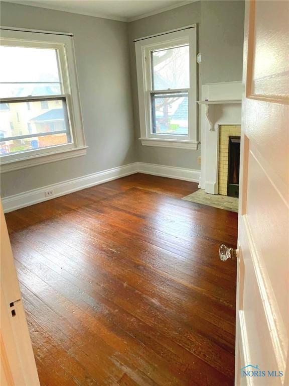 unfurnished living room featuring hardwood / wood-style flooring, a fireplace with flush hearth, and baseboards