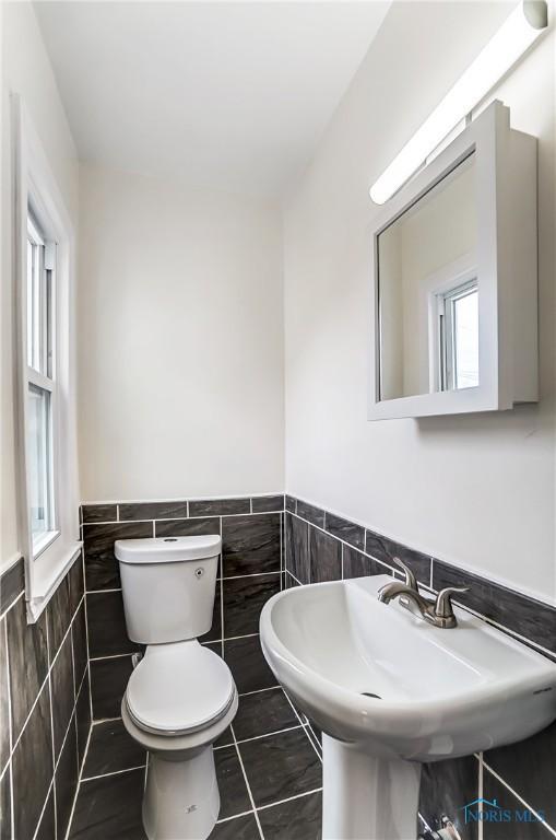 bathroom with a sink, tile patterned flooring, wainscoting, tile walls, and toilet