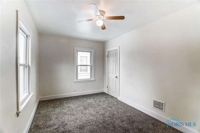 empty room featuring plenty of natural light, dark carpet, visible vents, and baseboards