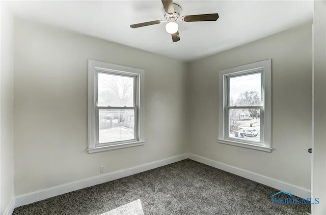 spare room featuring a wealth of natural light, dark carpet, baseboards, and ceiling fan