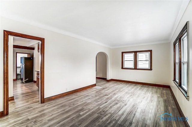 empty room with baseboards, arched walkways, and wood finished floors