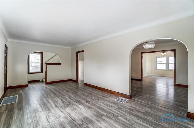 spare room featuring wood finished floors, arched walkways, visible vents, and baseboards