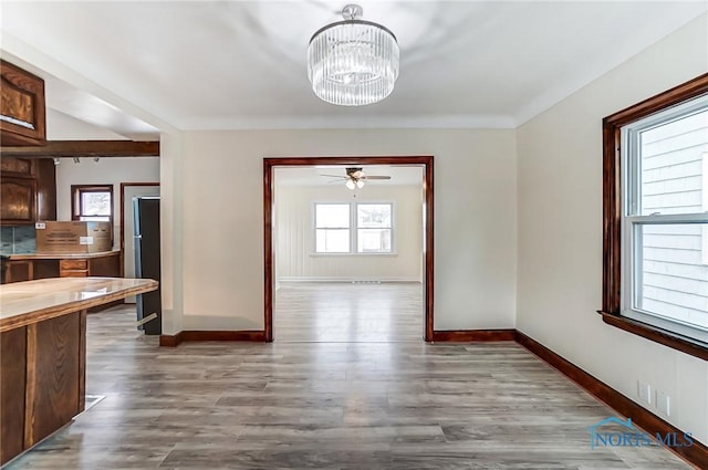 unfurnished dining area featuring baseboards, wood finished floors, and ceiling fan with notable chandelier