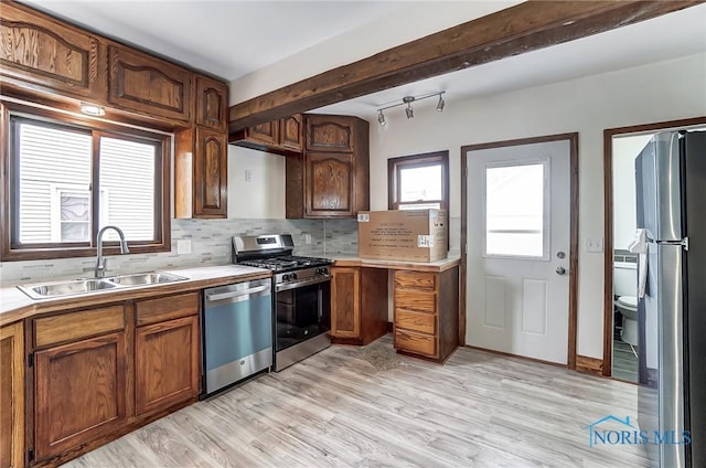 kitchen featuring backsplash, light wood-type flooring, light countertops, appliances with stainless steel finishes, and a sink