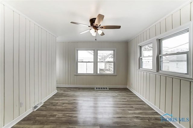 empty room featuring dark wood-type flooring, baseboards, visible vents, and ceiling fan