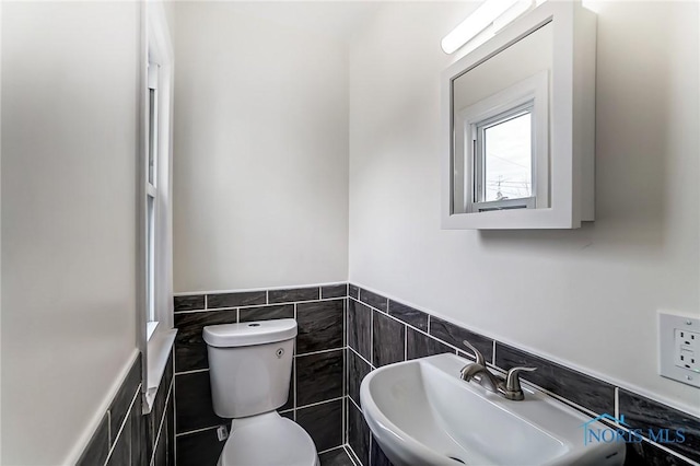 bathroom featuring a sink, a wainscoted wall, toilet, and tile walls