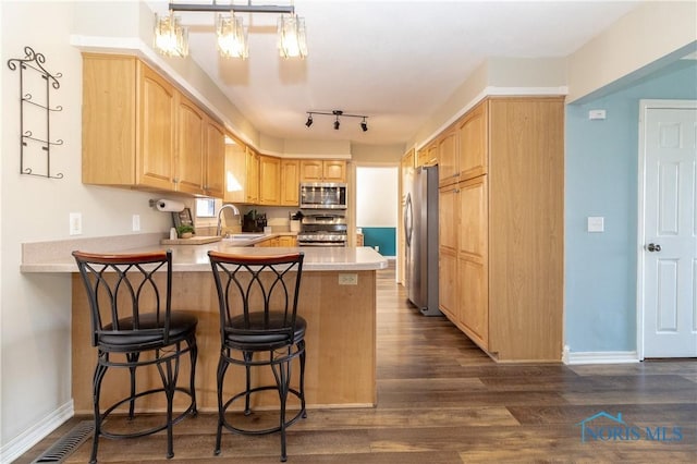 kitchen featuring light brown cabinets, dark wood finished floors, stainless steel appliances, a peninsula, and light countertops