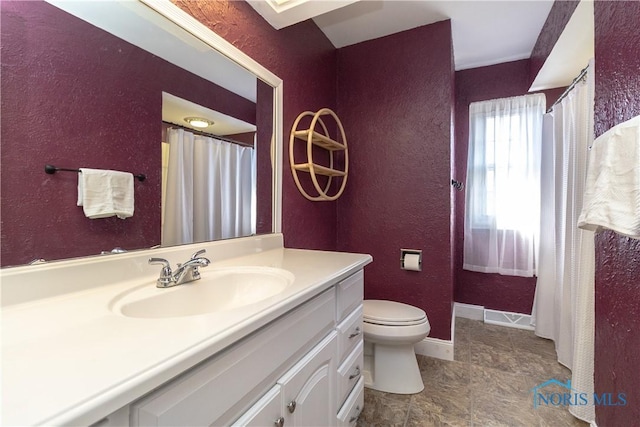 bathroom featuring baseboards, toilet, vanity, and a textured wall