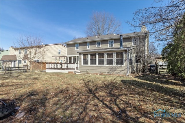 rear view of house featuring a wooden deck, a yard, a chimney, and fence