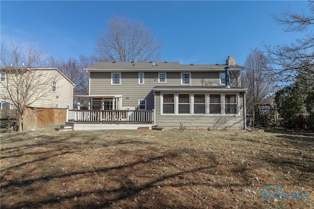 back of property featuring a yard, a deck, a chimney, and fence