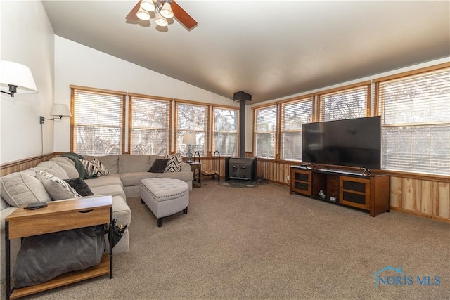 carpeted living area with lofted ceiling, ceiling fan, and a wood stove