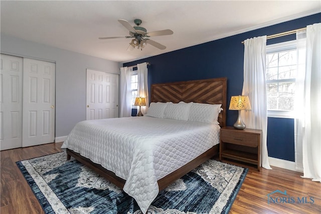 bedroom with wood finished floors, baseboards, two closets, and ceiling fan