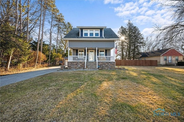 bungalow-style home featuring covered porch, a shingled roof, a front yard, and fence