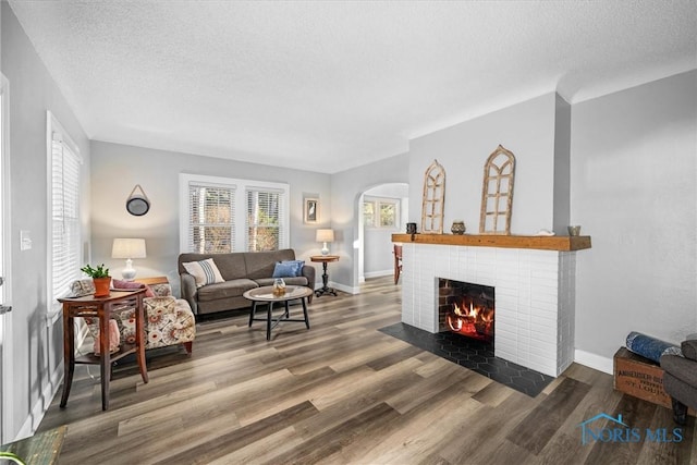 living area with a brick fireplace, wood finished floors, arched walkways, and a wealth of natural light