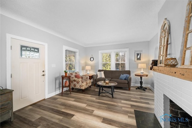 living area with baseboards, a textured ceiling, a brick fireplace, and wood finished floors