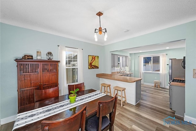 dining area with an inviting chandelier, baseboards, light wood-type flooring, and a textured ceiling