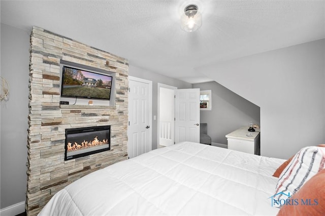 bedroom featuring baseboards, a large fireplace, and a textured ceiling