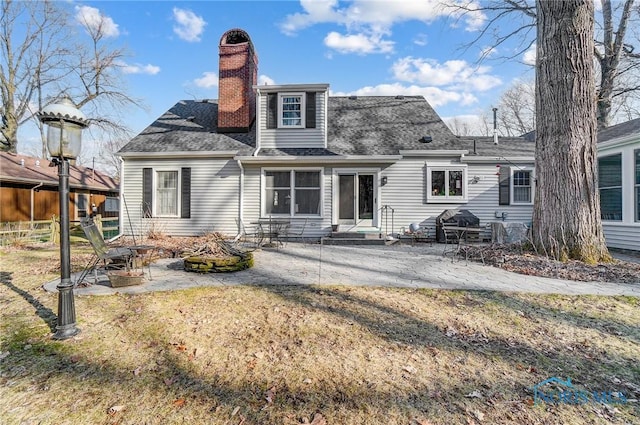 rear view of house with a patio area, a lawn, roof with shingles, and a chimney