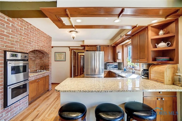 kitchen with a peninsula, open shelves, brown cabinetry, and appliances with stainless steel finishes