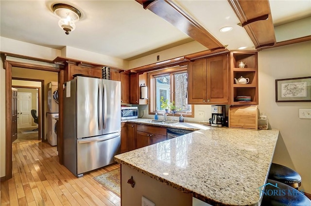 kitchen featuring stacked washer and clothes dryer, open shelves, stainless steel appliances, a peninsula, and brown cabinetry